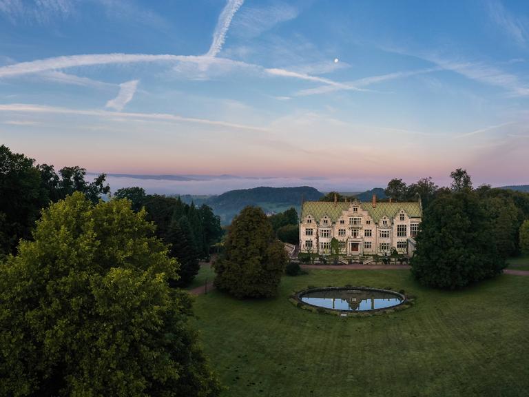 Drohnenblick über das Schloss  und den Landschaftspark Altenstein mit gefärbtem Abendhimmel.