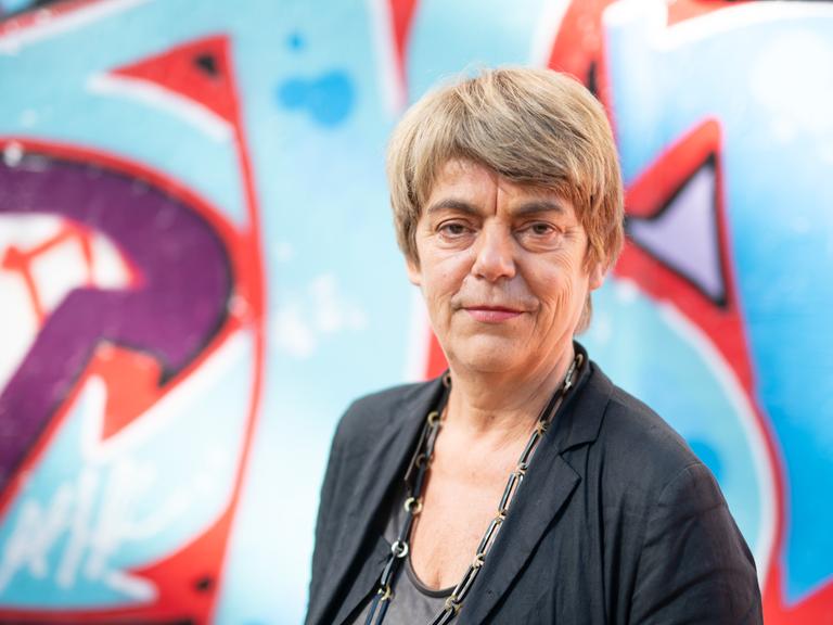 Amelie Deuflhard, die Intendantin der Kulturfabrik Kampnagel, steht vor einer mit Graffiti besprüh
ten Wand und blickt in die Kamera