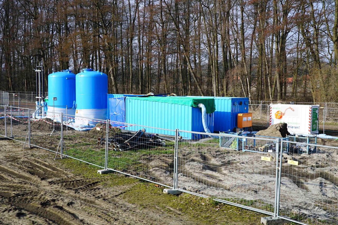 Auf einem eingezäunten Gelände in der Nähe einer Baumgruppe stehen Baumaschinen und runde blaue Tanks. Auf einem eingezäunten Gelände in der Nähe einer Baumgruppe stehen Baumaschinen und runde blaue Tanks.