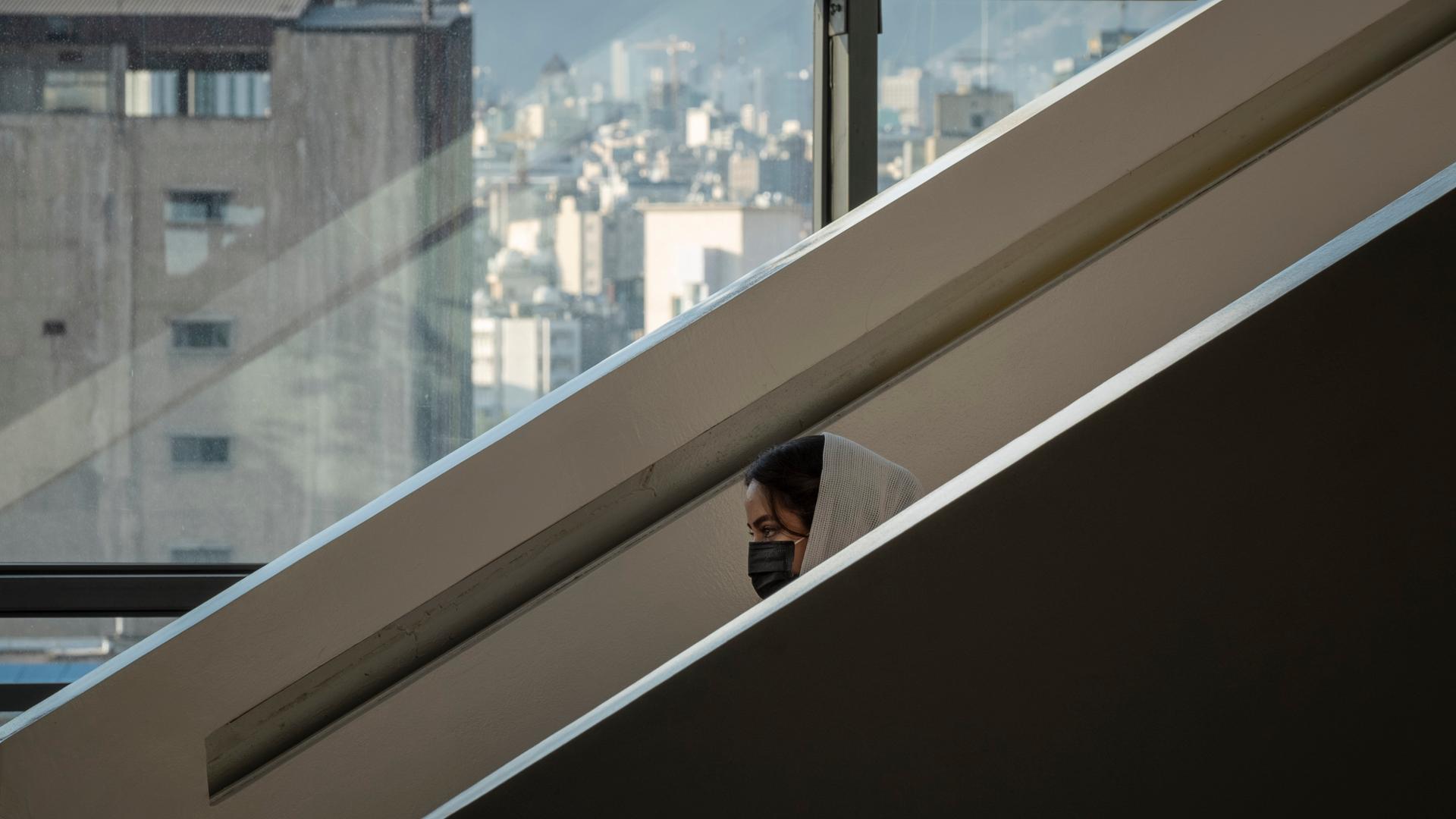 Eine Frau steht auf einer Rolltreppe in einer Mall in Teheran. Sie fährt abwärts und hinter einer Mauer ragt nur ihr Kopf hervor. Eine Frau steht auf einer Rolltreppe in einer Mall in Teheran. Sie fährt abwärts und hinter einer Mauer ragt nur ihr Kopf hervor.