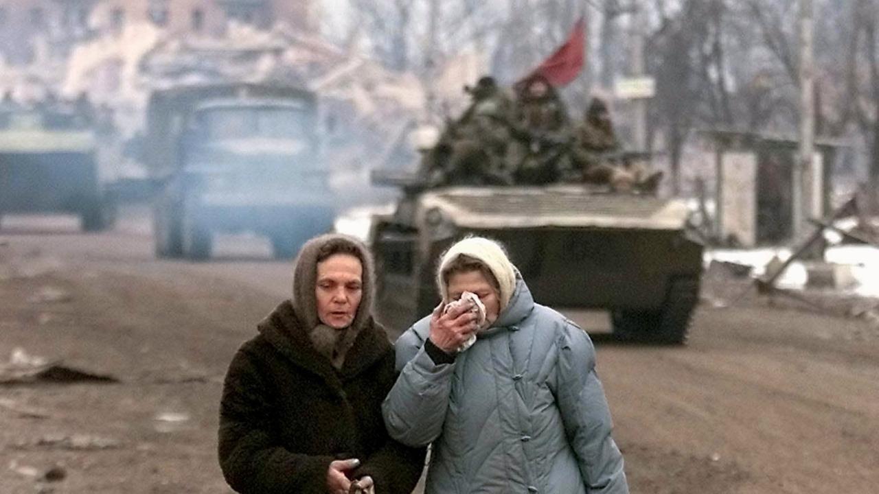 Zwei tschetschenische Frauen im Februar 2000 in der fast völlig zerstörten Stadt Grosny. Im Hintergrund rollt ein russischer Armee-Konvoi durch die Stadt.
