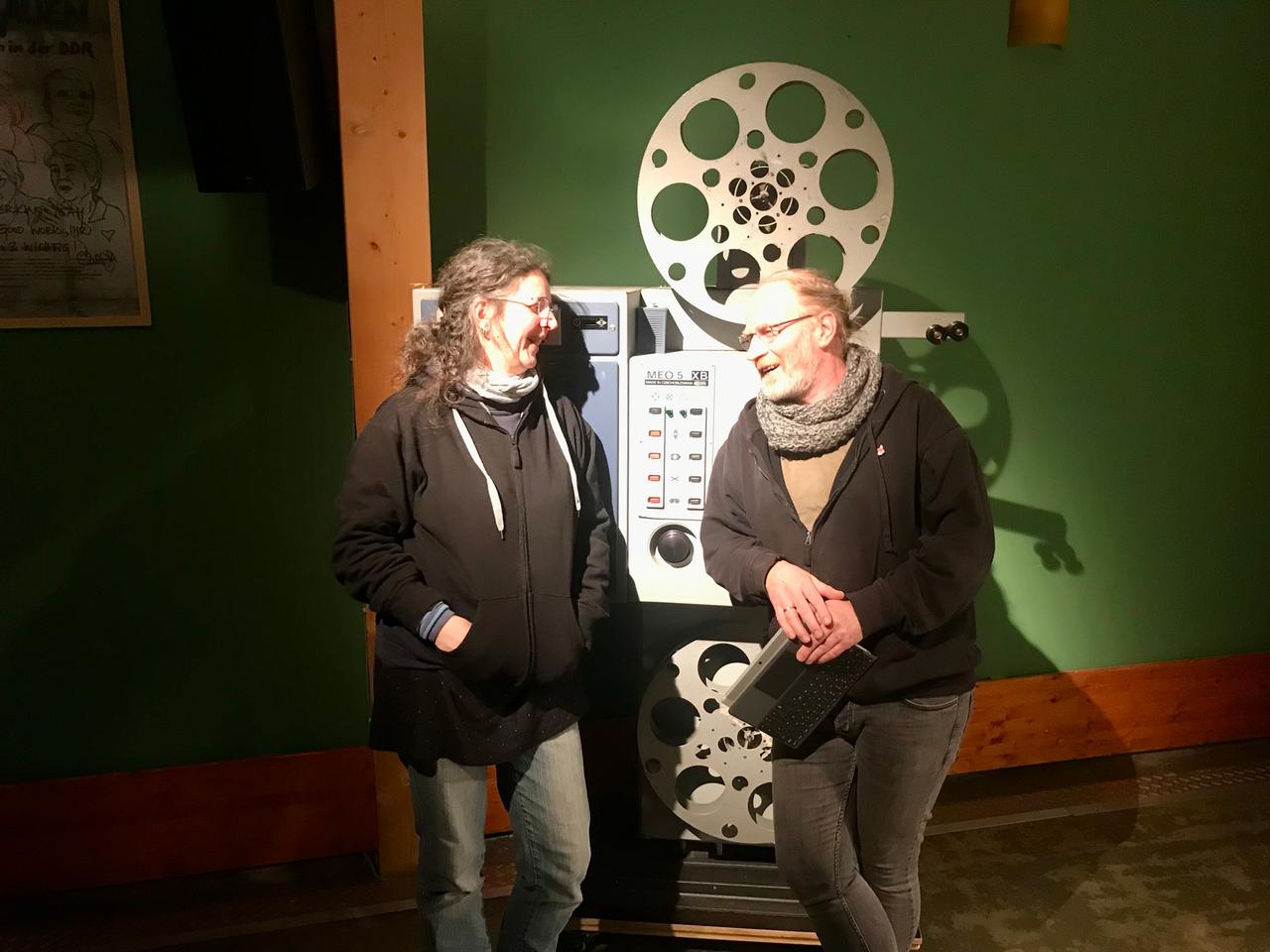 Antje Schadow aus dem Vorstand des vom Kunstbauerkinos in Großhennersdorf und Filmvorführer Thomas Fux  stehen vor einem Kinoprojektor.