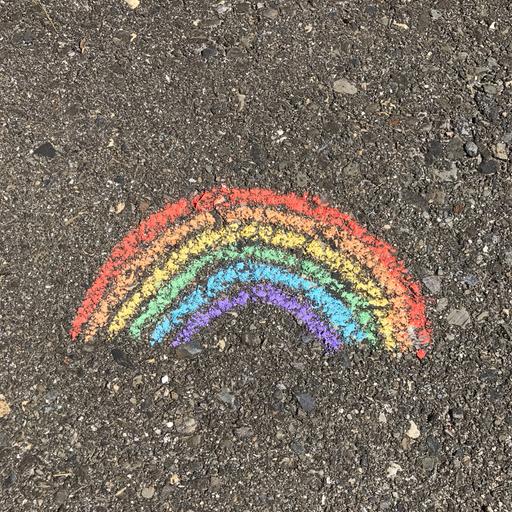 Ein Regenbogen mit Kreide auf den Asphalt gemalt.
