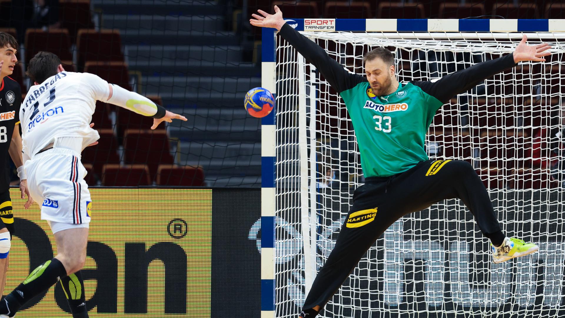Ein Spieler von Frankreich wirft den Ball in das Tor. Der Tor-Hüter von Deutschland springt in die Luft und streckt die Arme aus. Ein Spieler von Frankreich wirft den Ball in das Tor. Der Tor-Hüter von Deutschland springt in die Luft und streckt die Arme aus.