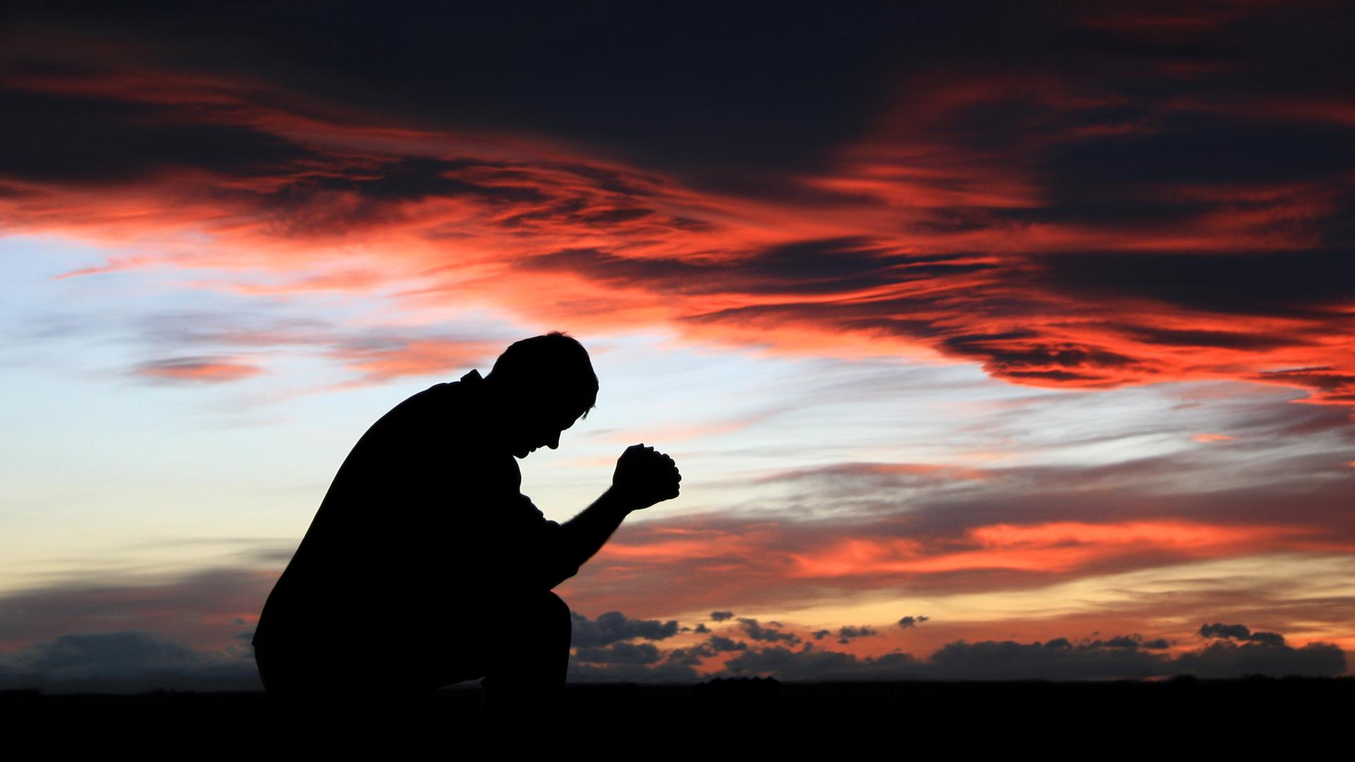 Ein Mann betet gegen den dramatischen Sonnenuntergang.