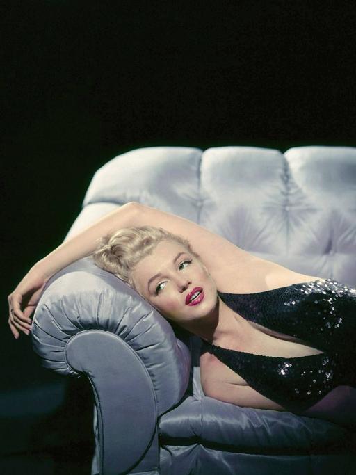 Marilyn Monroe liegt elegant in ihrem Abendkleid auf einem Sofa.