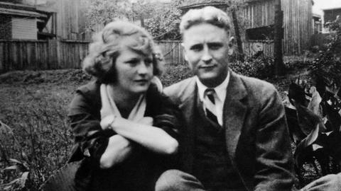 Schwarzweißfoto von F. Scott Fitzgerald und seiner Ehefrau Zelda, die auf dem Boden eines Gartens sitzen