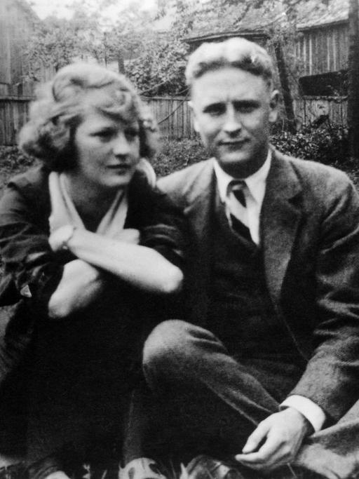 Schwarzweißfoto von F. Scott Fitzgerald und seiner Ehefrau Zelda, die auf dem Boden eines Gartens sitzen