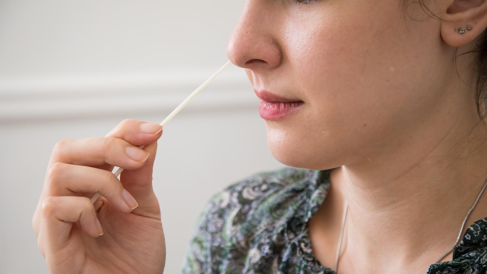 Eine Frau führt ein Teststäbchen in die Nase (gestellte Szene) Eine Frau führt ein Teststäbchen in die Nase (gestellte Szene)