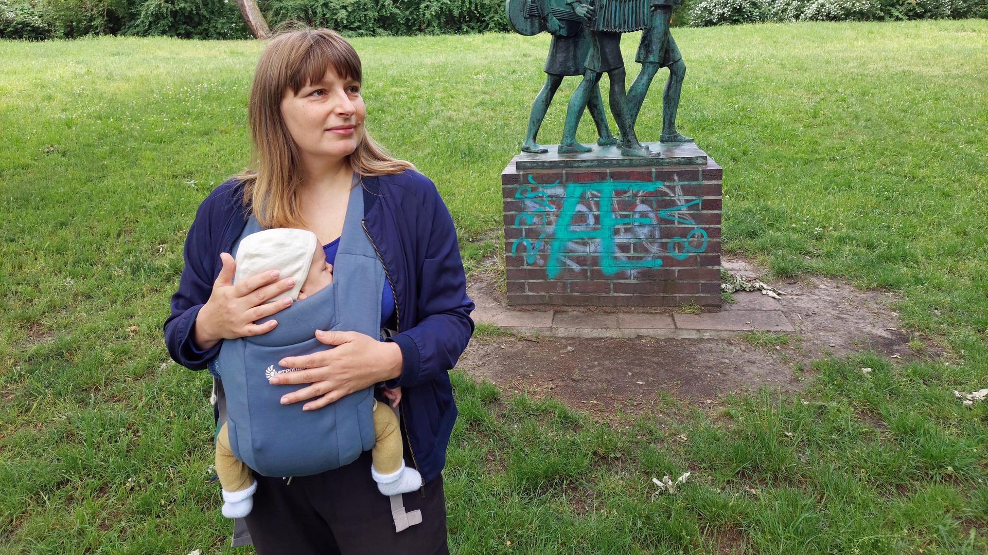 Eine junge Frau mit einem Baby im Tragetuch in einem Park Eine junge Frau mit einem Baby im Tragetuch in einem Park