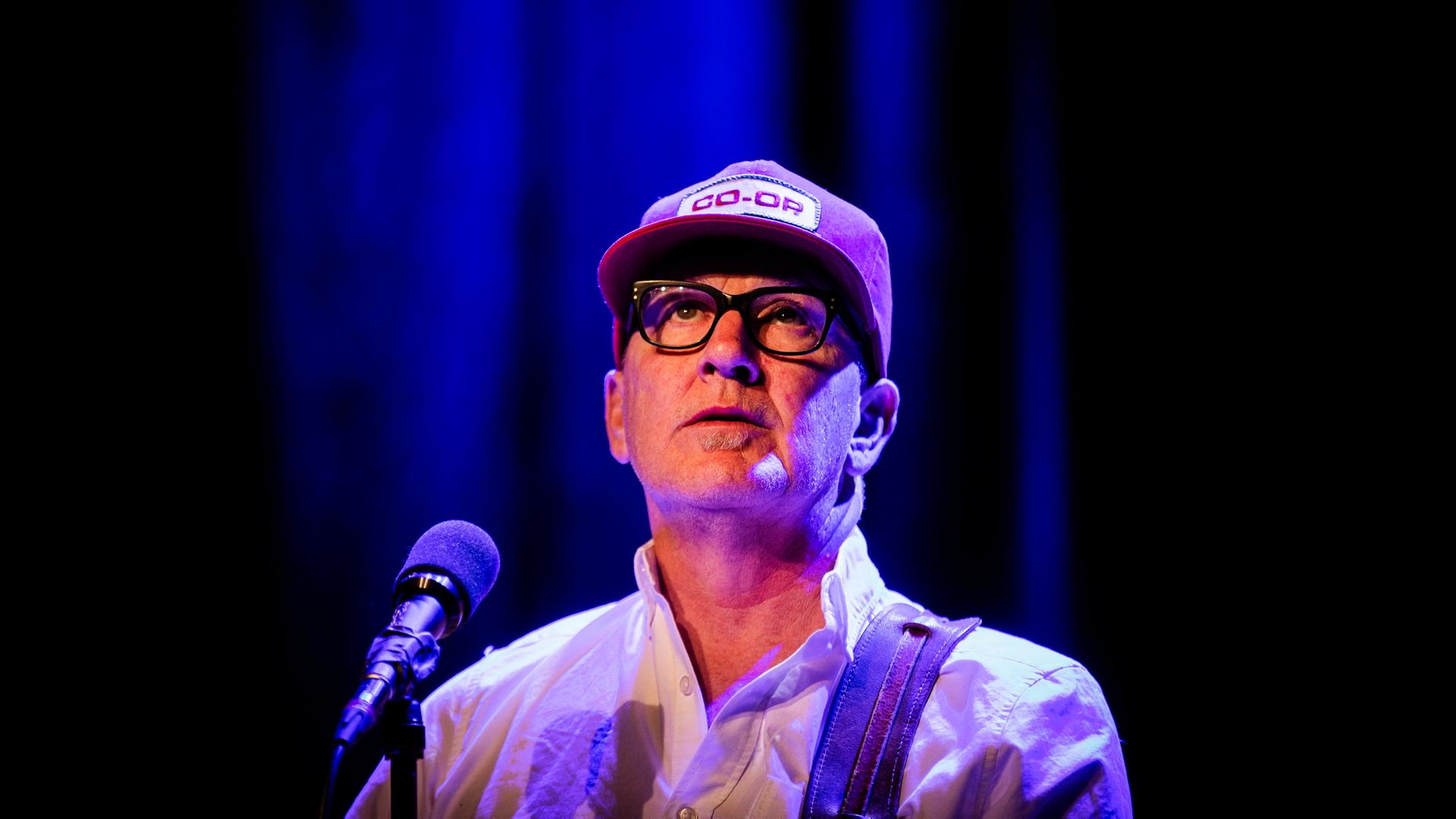 Kurt Wagner, Sänger der Band Lambchop steht auf einer blauviolett erleuchteten Bühne am Mikrofon und schaut nach oben