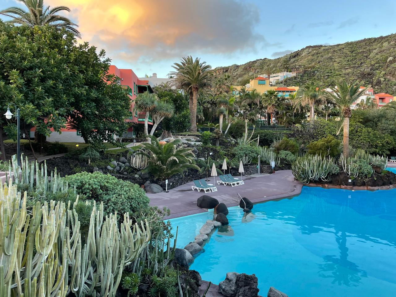 Ein idyllischer Hotelpool mit Palmen und Liegen drumherum. Im Hintergrund der vom Vulkan rotgefärbte Himmel. Ein idyllischer Hotelpool mit Palmen und Liegen drumherum. Im Hintergrund der vom Vulkan rotgefärbte Himmel.