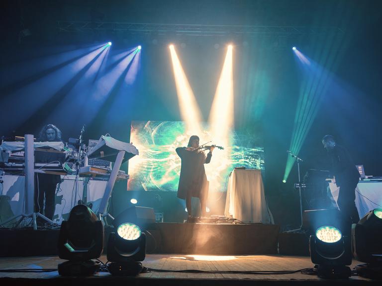 Die drei Mitglieder von Tangerine Dream performen auf einer grün-blau beleuchteten Bühne.