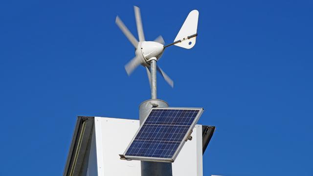 Weiße Miniwindräder und Solar Panels auf einem Häuserdach vor blauem Himmel.