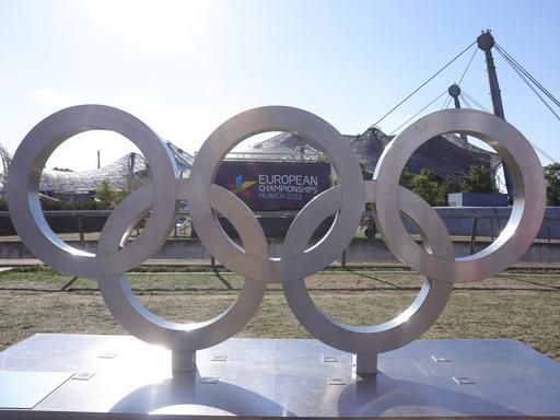 Olympische Ringe stehenin München vor dem Plakat der European Championships