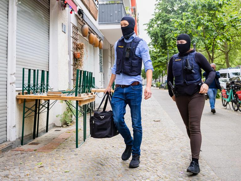 Zwei Polizisten gehen bei einer Hausdurchsuchung in Berlin-Kreuzberg zu einem Gebäude. 