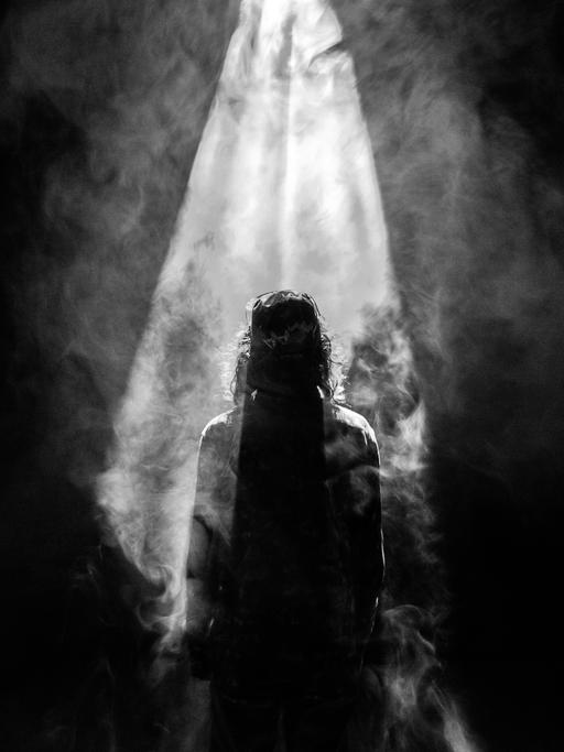 Ein ikonografisches Schwarz-Weiß-Bild einer Jesusfigur, von hinten gesehen, vor hellem Licht, das von oben auf sie herabscheint.