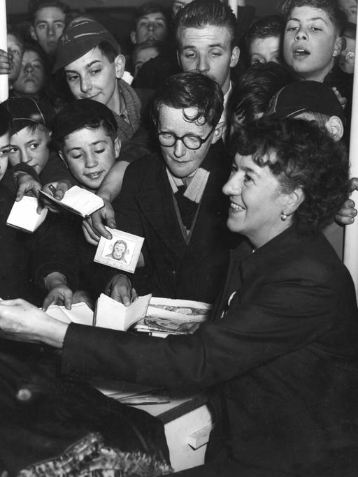 Die britische Kinderbuchautorin Enid Blyton inmitten von Kindern bei einer Autogrammstunde in London 1953.