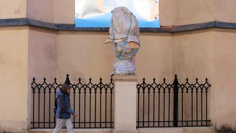 Eine Passantin geht an einer verhüllten und verpackten Statue vorbei.