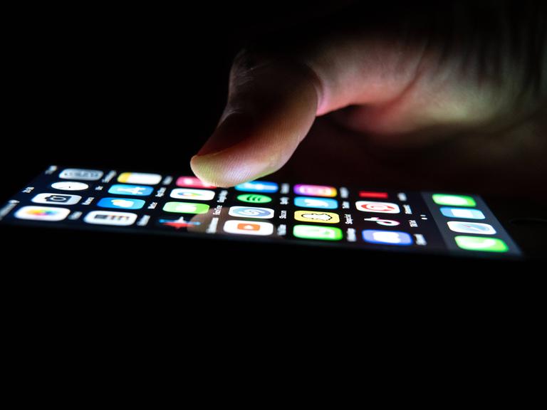 Ein Mann hält ein iPhone in seiner Hand, auf dem Application Apps zu sehen sind. 