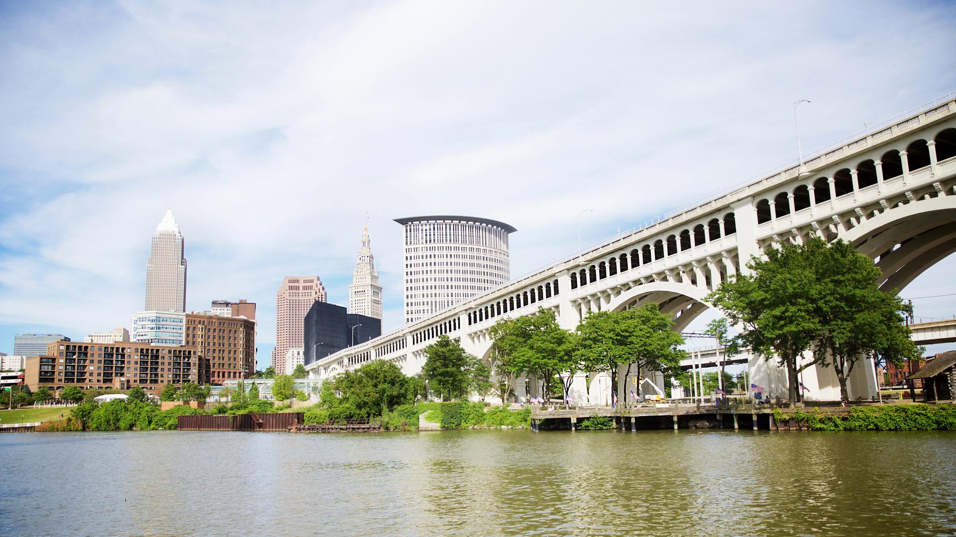 Die Skyline von Cleveland in Ohio, vom Heritage Park aus gesehen mit Brücke übers Wasser und Bäumen Die Skyline von Cleveland in Ohio, vom Heritage Park aus gesehen mit Brücke übers Wasser und Bäumen