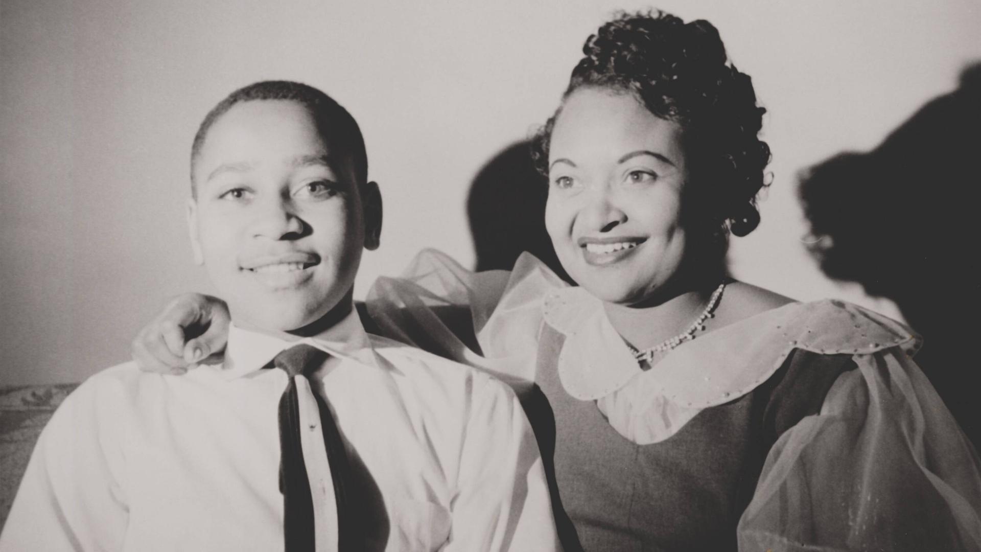 Schwarzweiß-Familienschnappschuss: Emmett Till sitzt fröhlich neben seiner Mutter Mamie Bradley, die freundlich lacht. Schwarzweiß-Familienschnappschuss: Emmett Till sitzt fröhlich neben seiner Mutter Mamie Bradley, die freundlich lacht.