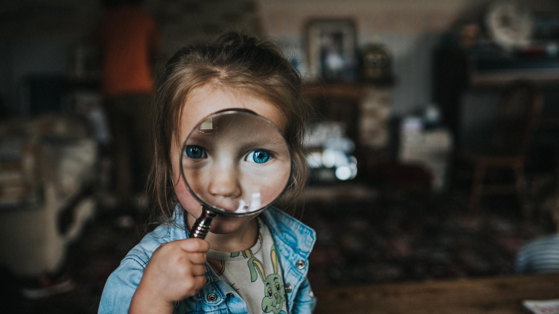 Ein Kind schaut durch eine Lupe. Das Auge ist entsprechend stark vergrößert.