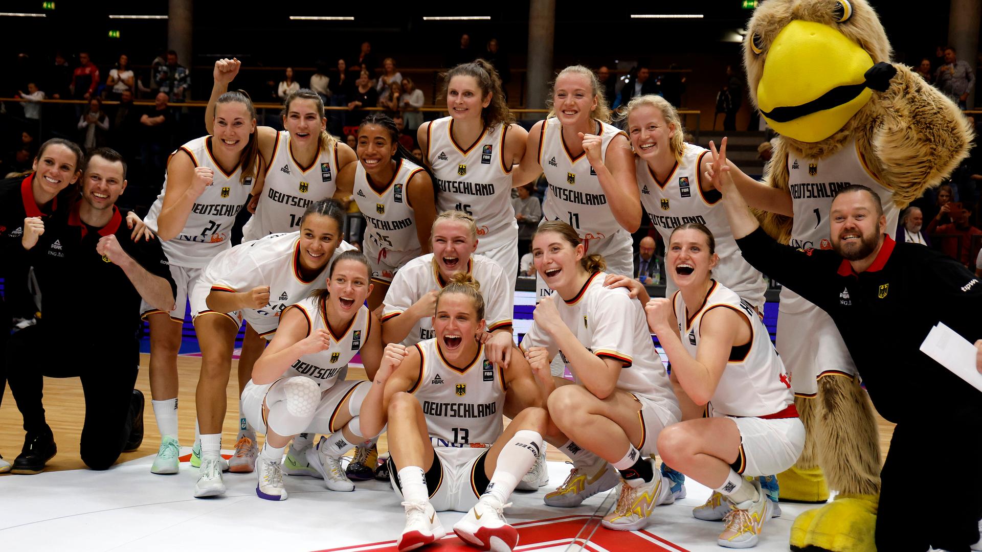 Die deutschen Basketball-Spielerinnen sitzen in einem Halbkreis auf dem Boden und jubeln über ihren Sieg.
