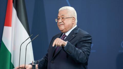 Mahmoud Abbas steht vor einem Mikrofon, in Hintergrund die palästinensische Flagge.
