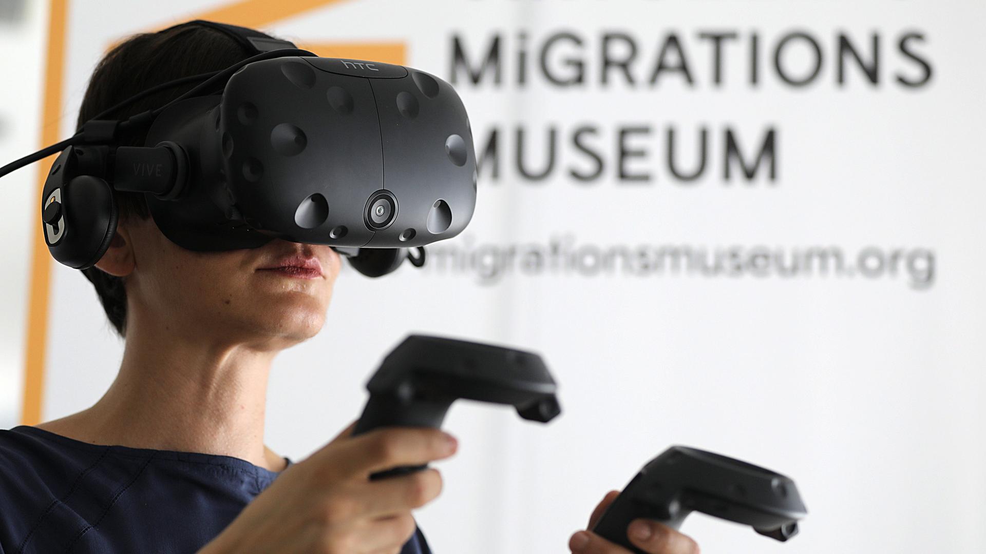 Eine Mitarbeiterin steht mit einer VR-Brille im Virtuellen Migrationsmuseum in Köln. Besucher des Museums können sich anhand digitaler Straßenszenen, Gebäuden und Objekten mit der Migrationsgeschichte auseinandersetzten. Dafür werden Virtual-Reality-Brillen (VR) genutzt. Eine Mitarbeiterin steht mit einer VR-Brille im Virtuellen Migrationsmuseum in Köln. Besucher des Museums können sich anhand digitaler Straßenszenen, Gebäuden und Objekten mit der Migrationsgeschichte auseinandersetzten. Dafür werden Virtual-Reality-Brillen (VR) genutzt.