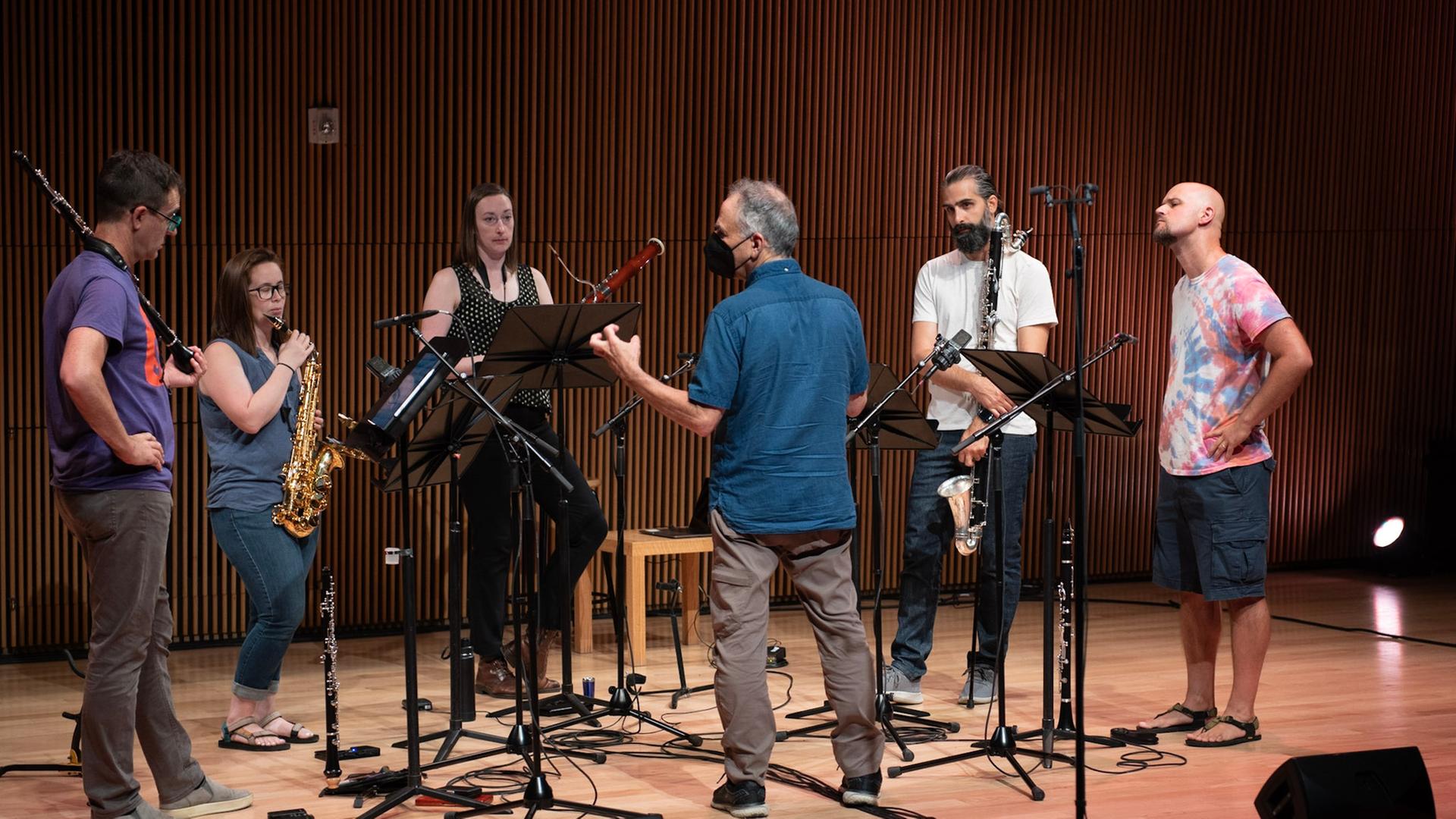 Die 5 Musiker des Ensembles stehen mit ihren Instrumenten auf der Bühne während der Komponist ihnen etwas erklärt