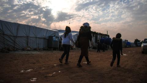 Drei Kinder sind von hinten dabei zu sehen wie sie durch ein Flüchtlingscamp laufen.
