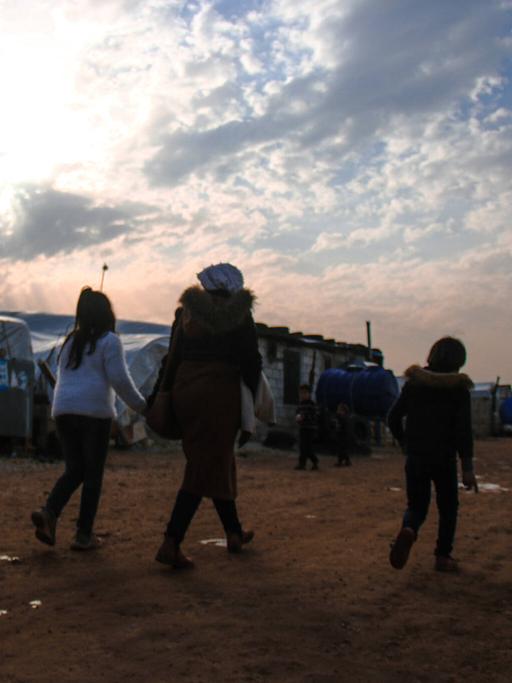 Drei Kinder sind von hinten dabei zu sehen wie sie durch ein Flüchtlingscamp laufen.