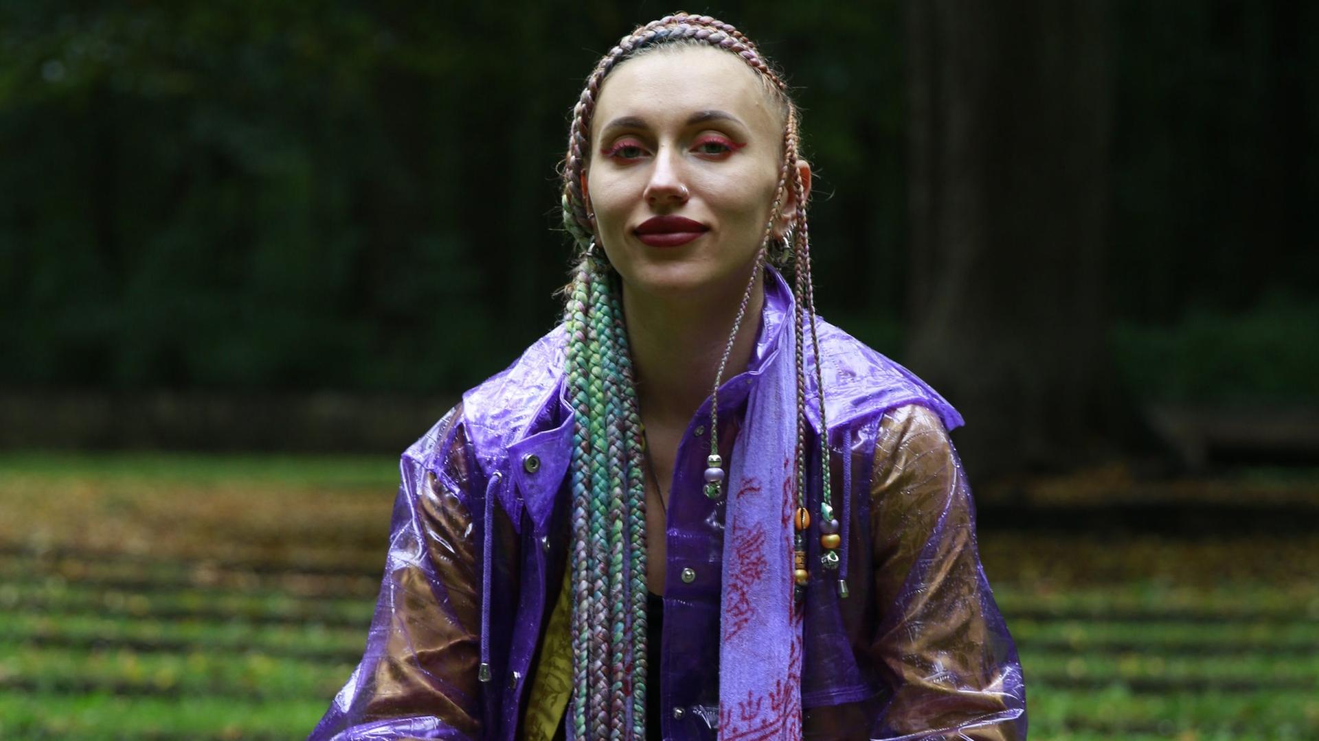 Die Haarflechtkünstlerin Angela Delgado hockt auf einer Wiese und blickt in die Kamera. Die Haarflechtkünstlerin Angela Delgado hockt auf einer Wiese und blickt in die Kamera.