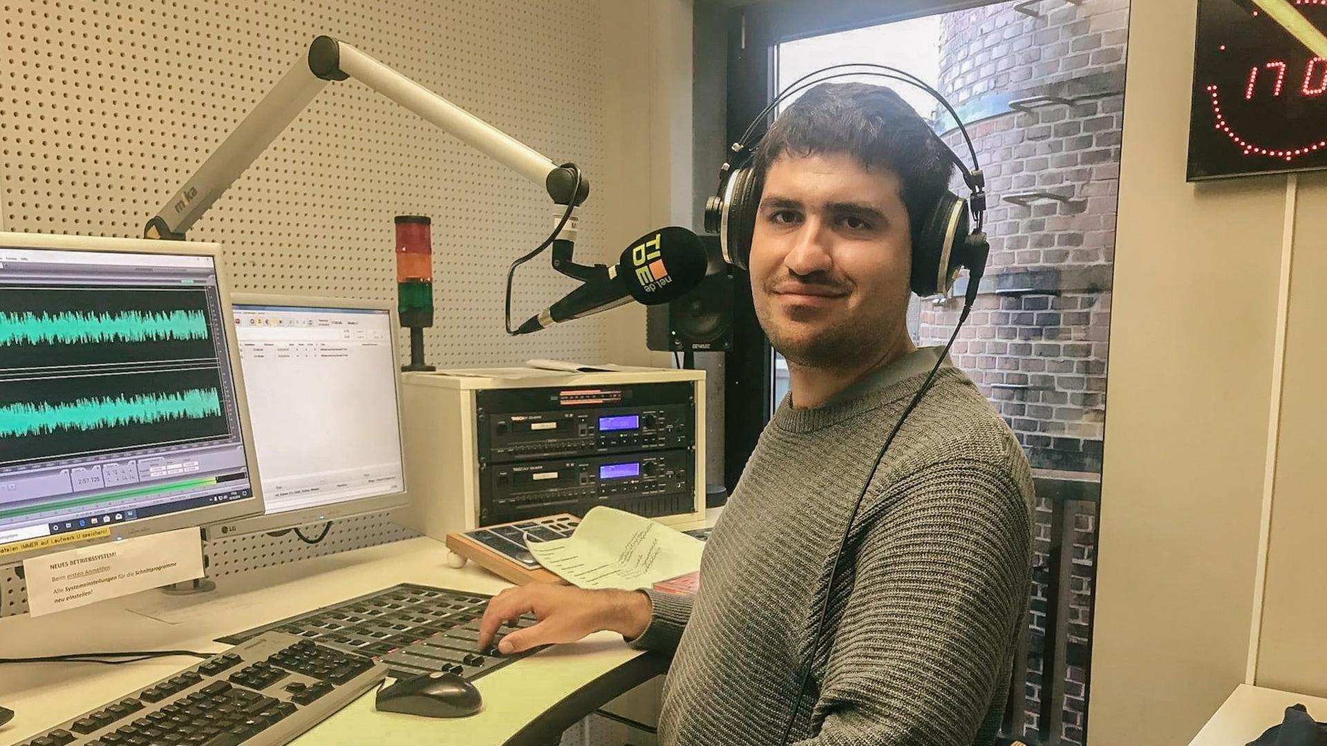 Ein junger Mann mit Kopfhörern auf dem Kopf in einem Radiostudio vor dem Computer Ein junger Mann mit Kopfhörern auf dem Kopf in einem Radiostudio vor dem Computer