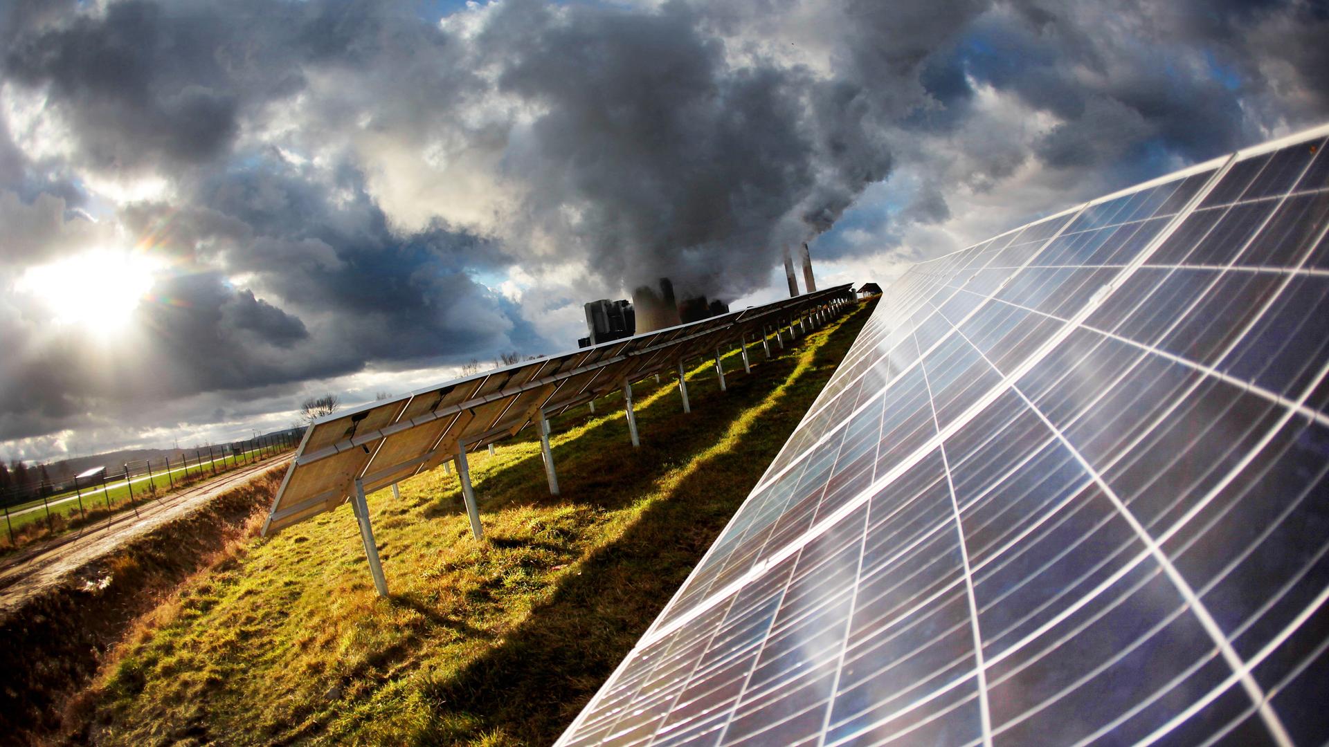 Eine Solaranlage auf der grünen Wiese. Im Hintergrund rauchen die Schlote eines Kraftwerks. Eine Solaranlage auf der grünen Wiese. Im Hintergrund rauchen die Schlote eines Kraftwerks.