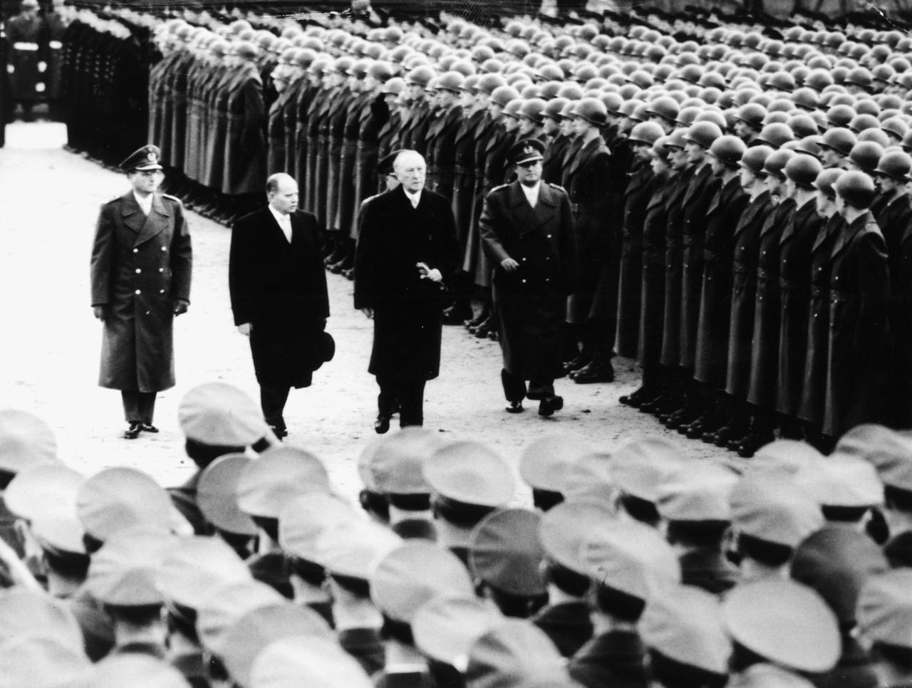Adenauer und Militaärangehörige laufen auf diesem Schwarz-Weiß-Foto an Soldaten der Bundeswehr vorbei.