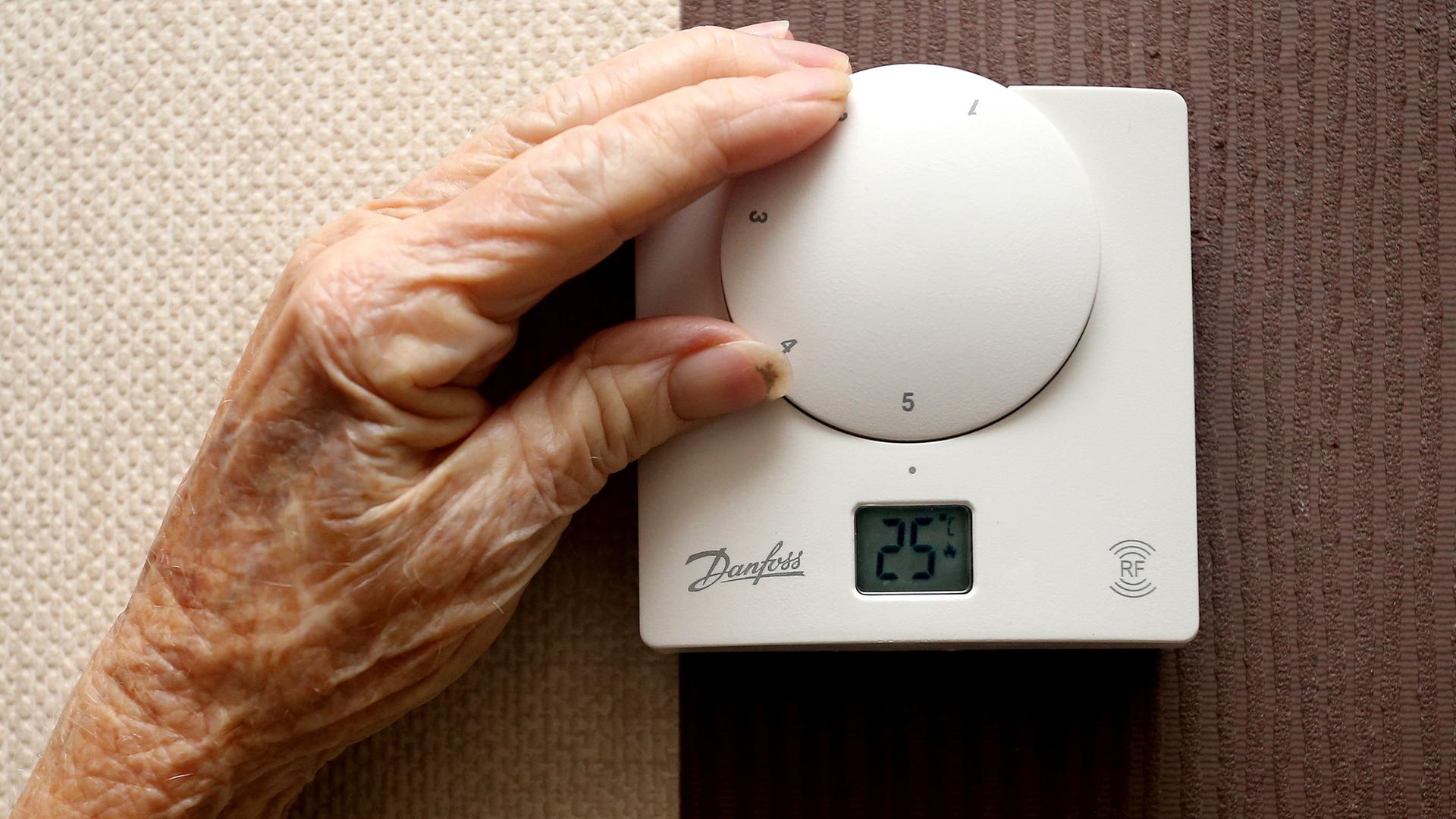 Die Hand einer älteren Frau bedient ein Thermostat