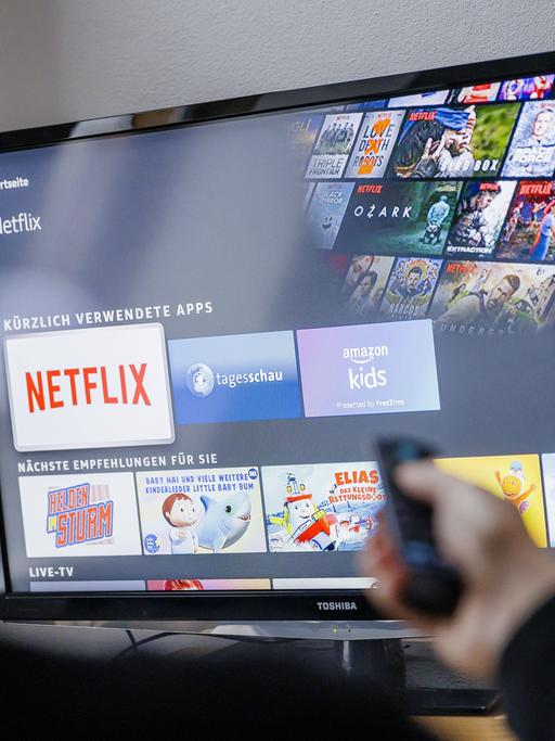 Auf einem TV-Bildschirm sind Logos von Medienplattformen zu sehen, darunter hervorgehoben dasjenige von Netflix.