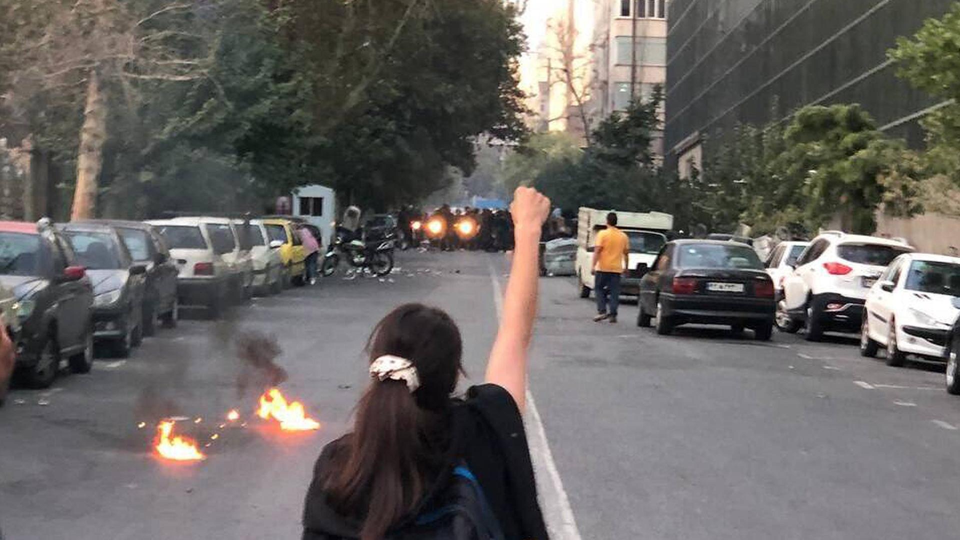 Während Portesten in der iranischen Hauptstadt Teheran streckt eine Person mi langen Haaren Polizeikräften die erhobene Faust entgegen. 