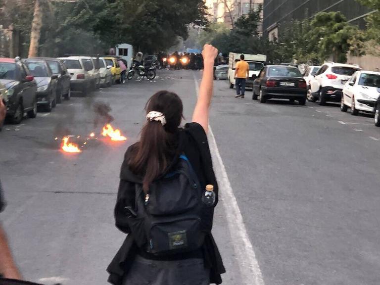 Während Portesten in der iranischen Hauptstadt Teheran streckt eine Person mi langen Haaren Polizeikräften die erhobene Faust entgegen. 