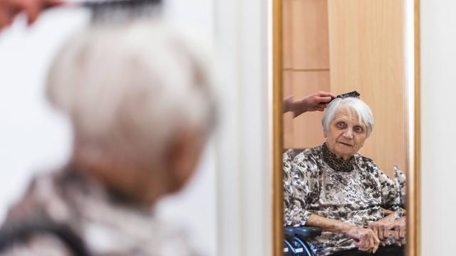 Eine Frau bürstet die Haare und kümmert sich um eine alte Frau. Symbolfoto Symbolfoto
