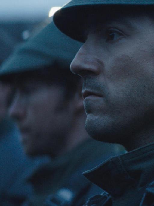 Im Still aus "Andor" ist Diego Luna in einer Großaufnahme im Profil zu sehen. Er scheint gemeinsam mit Soldaten in Reih und Glied zu stehen.