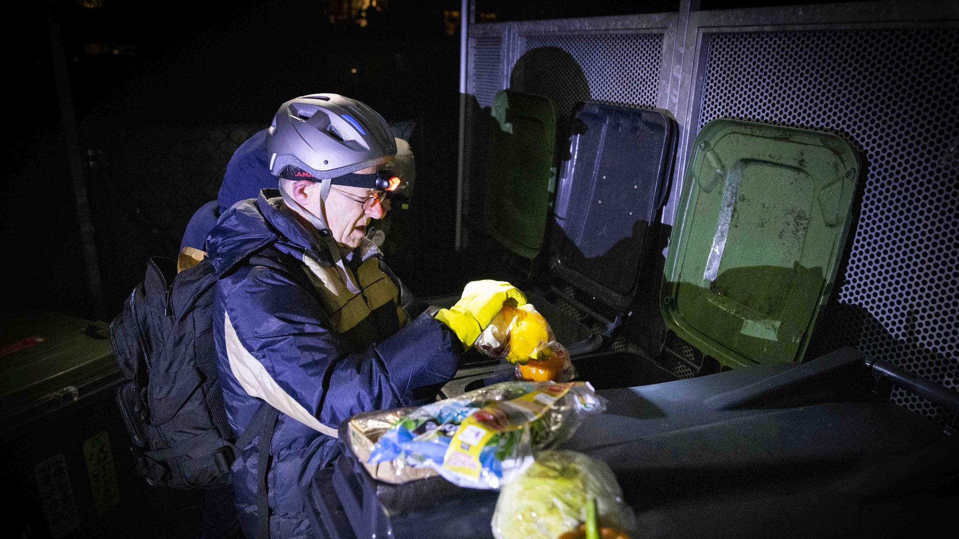 Der Jesuit Jörg Alt ist begleitet mit einer Outdoor-Jacke, er träg auch einen Helm und eine Stirnlampe. Aus einer Mülltonne holt er Lebensmittel. Der Jesuit Jörg Alt ist begleitet mit einer Outdoor-Jacke, er träg auch einen Helm und eine Stirnlampe. Aus einer Mülltonne holt er Lebensmittel.