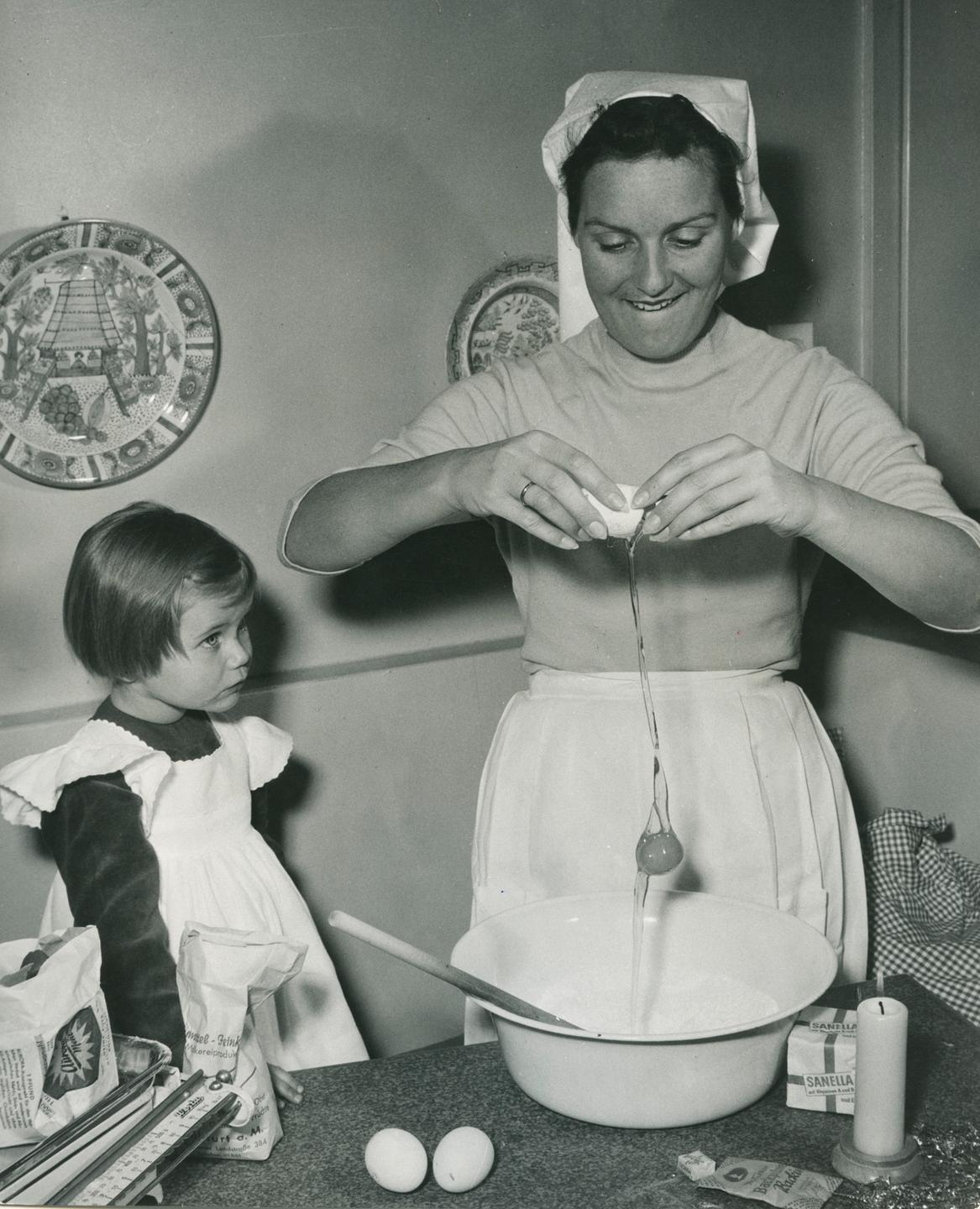 50er-Jahre: Ein Kind schaut einer Frau beim Backen zu.