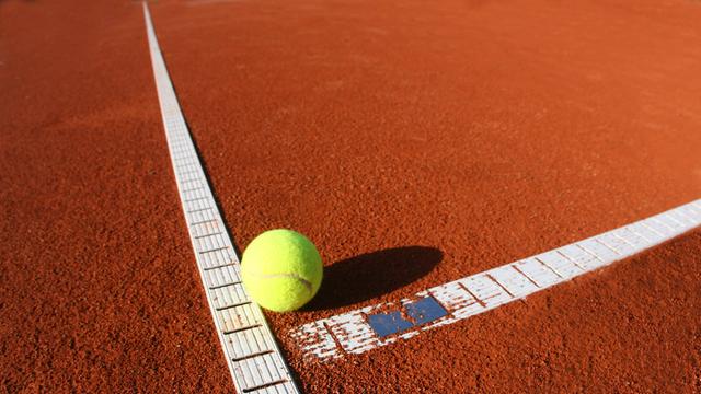 Ein Tennisball liegt auf einem Sandplatz 
