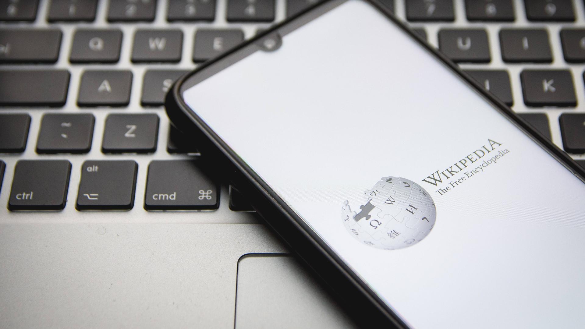 Ein Smartphone, auf dem Wikipedia aufgerufen ist, liegt auf einem Laptop. Ein Smartphone, auf dem Wikipedia aufgerufen ist, liegt auf einem Laptop.