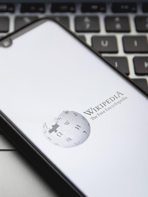 Ein Smartphone, auf dem Wikipedia aufgerufen ist, liegt auf einem Laptop.
