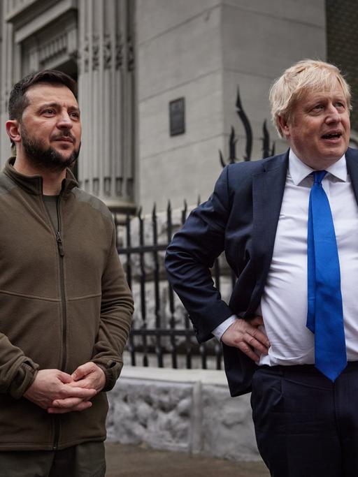 Der damalige britische Prime Minister Boris Johnson und der ukrainische Präsident Wolodymyr Selenskyi gehen über den Unabhängigkeitsplatz in Kiev. Der dunkelhaarige Selenskyi (links) hat einen olivgrünen Pullover an, der blonde Johnson trägt Anzug, weißes Hemd und Krawatte, die Hände stemmt er in die Hüfte.