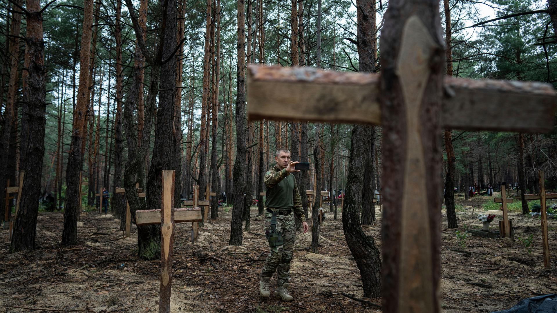 Ein Mann dokumentiert mit seinem Smartphone Gräber in einem Wald.